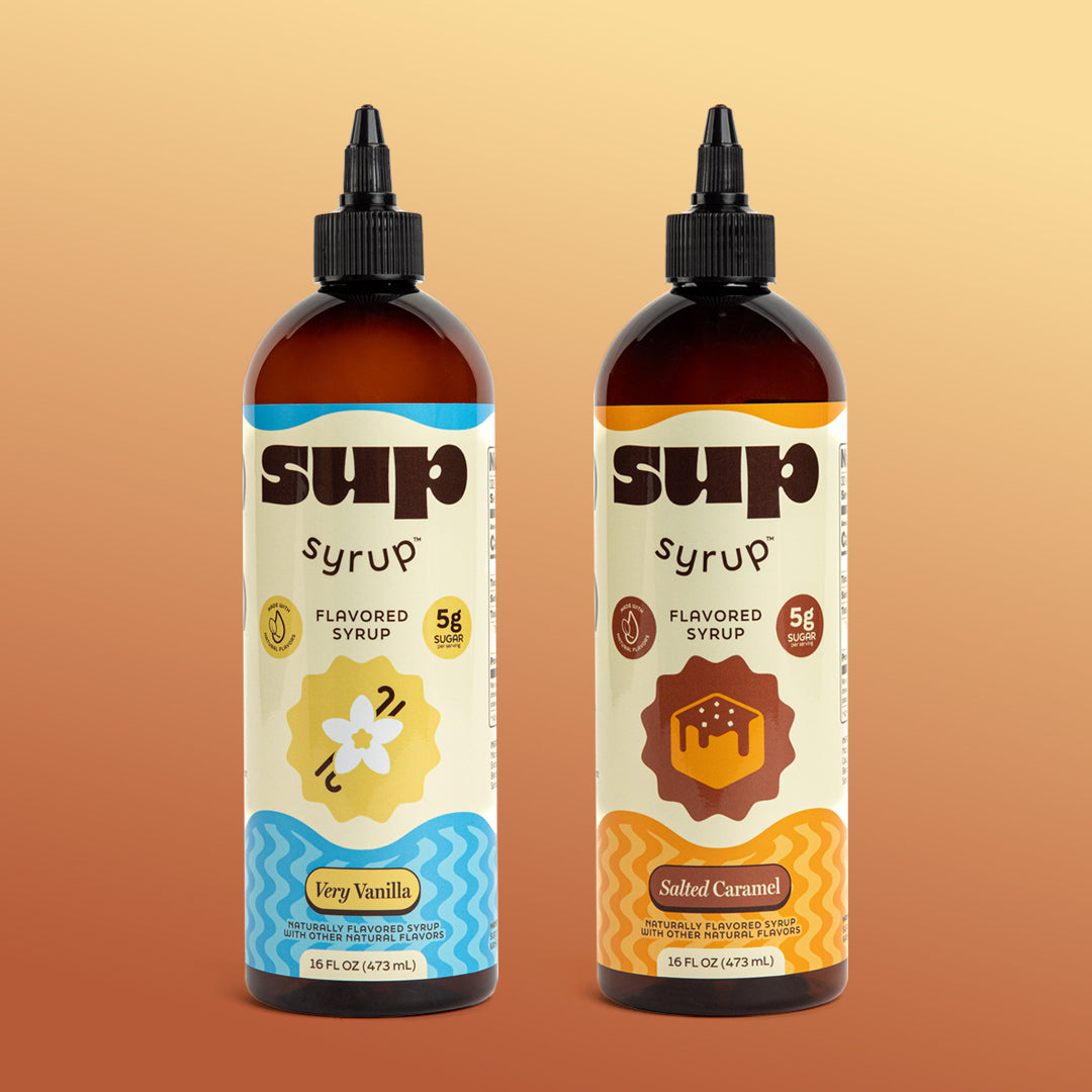 A 16 fl oz amber bottle of Sup Syrup Very Vanilla and Salted Caramel flavored syrup with black twist open caps, set against brown and yellow gradient background.