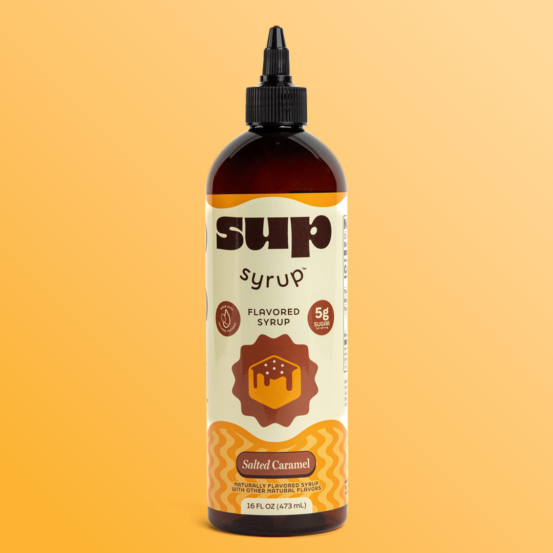 A 16 fl oz amber bottle of Sup Syrup Salted Caramel flavored syrup with a black twist open cap, set against an orange background.