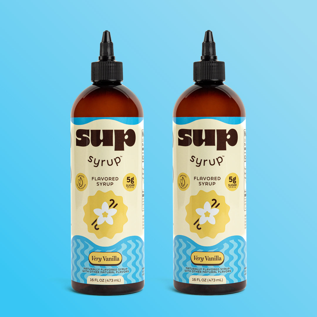 Two 16 fl oz amber bottles of Sup Syrup Very Vanilla flavored syrup with a black twist open cap, set against a solid light blue background.